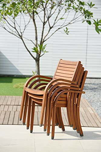 Stacked wooden chairs on a patio with a tree in the background.