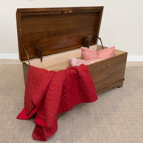 Open wooden chest with red quilt and pillows inside.