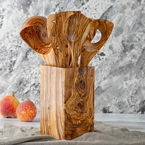 Wooden kitchen utensils in a wooden holder with peaches nearby.